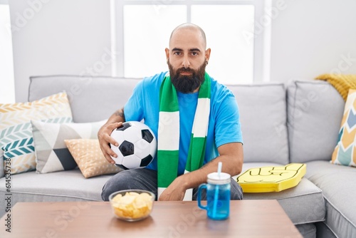 Young hispanic man with beard and tattoos football hooligan holding ball supporting team thinking attitude and sober expression looking self confident © Krakenimages.com