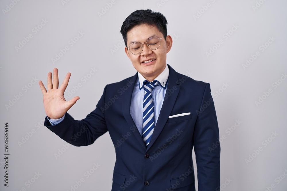 Young asian man wearing business suit and tie showing and pointing up with fingers number five while smiling confident and happy. Young asian man wearing business suit and tie showing and pointing up with fingers number five while smiling confident and happy.
