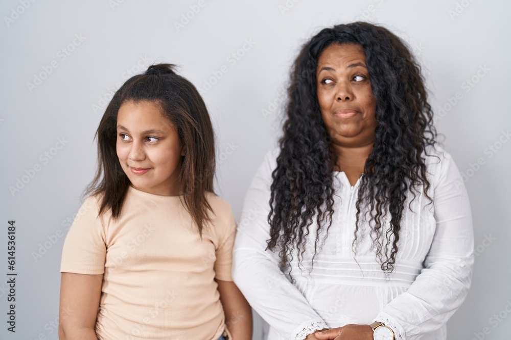 Mother and young daughter standing over white background smiling looking to the side and staring away thinking.