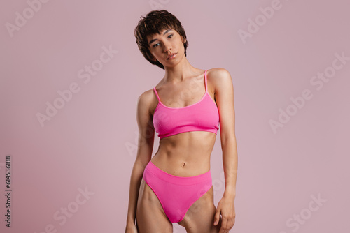 Beautiful young short hair woman in underwear standing against colored background