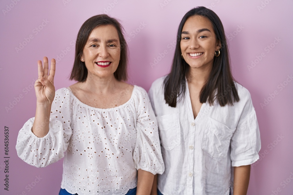 Hispanic mother and daughter together showing and pointing up with fingers number three while smiling confident and happy. Hispanic mother and daughter together showing and pointing up with fingers number three while smiling confident and happy.
