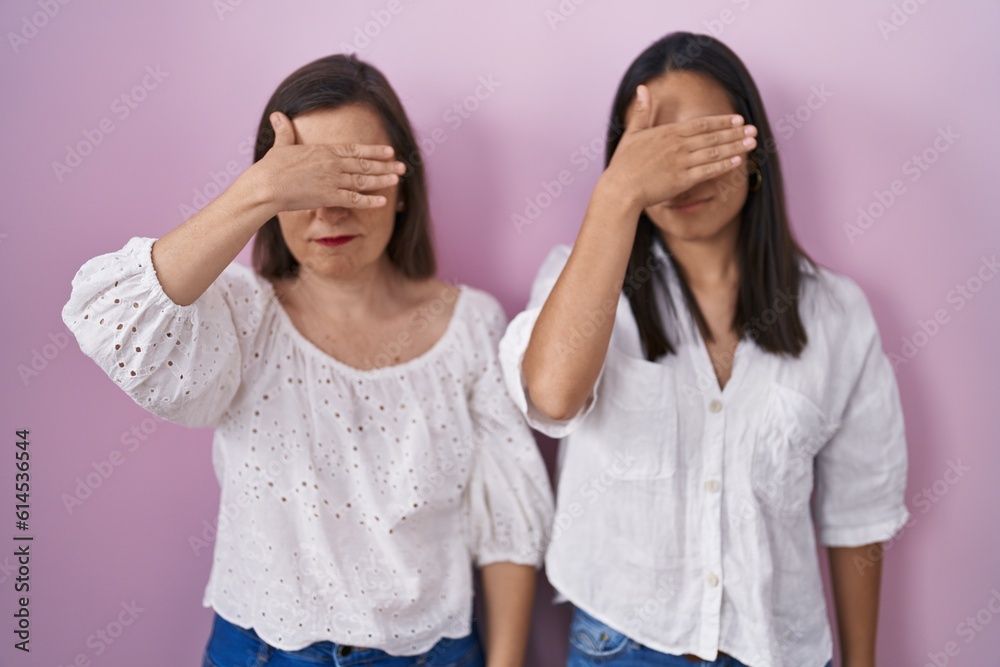 Hispanic mother and daughter together covering eyes with hand, looking serious and sad. sightless, hiding and rejection concept Hispanic mother and daughter together covering eyes with hand, looking serious and sad. sightless, hiding and rejection concept