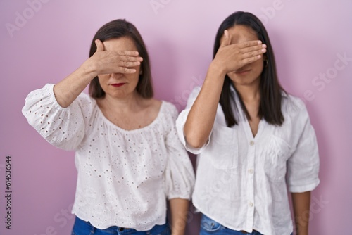 Hispanic mother and daughter together covering eyes with hand, looking serious and sad. sightless, hiding and rejection concept