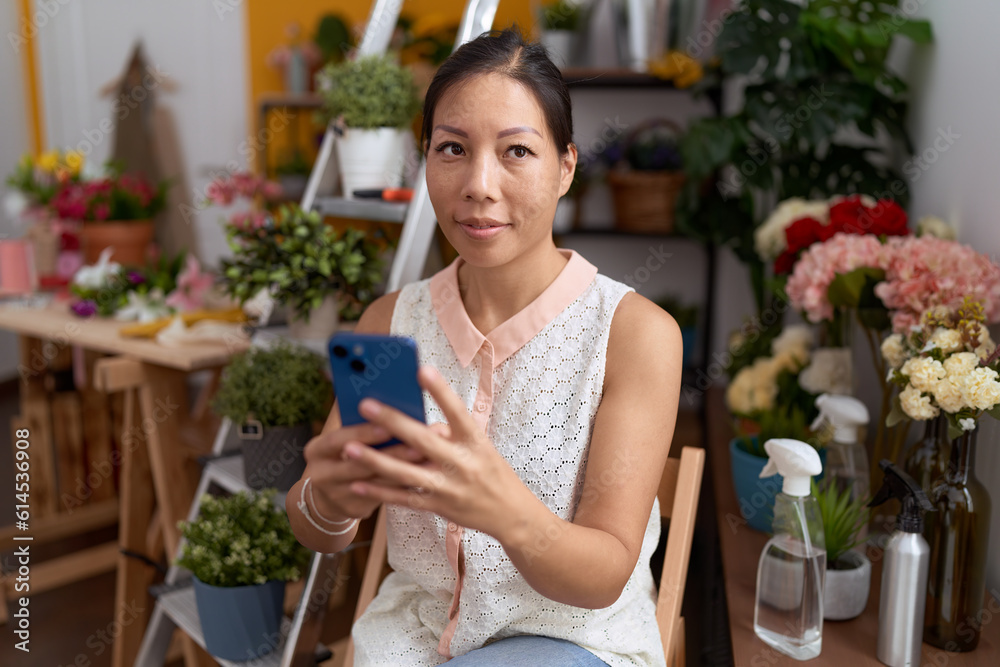 Young asian woman florist smiling confident using smartphone at flower shop