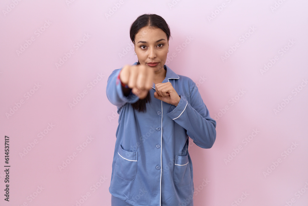 Young arab woman wearing blue pajama punching fist to fight, aggressive and angry attack, threat and violence Young arab woman wearing blue pajama punching fist to fight, aggressive and angry attack, threat and violence