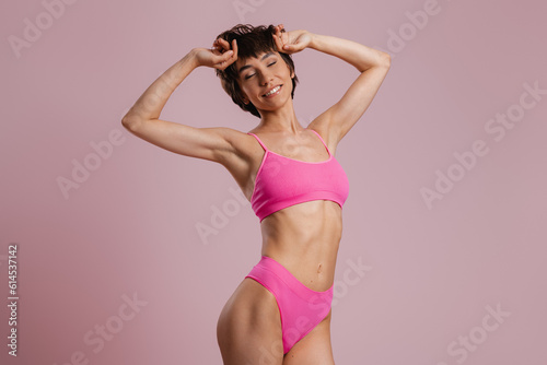 Beautiful young fit woman in underwear looking happy while standing against colored background