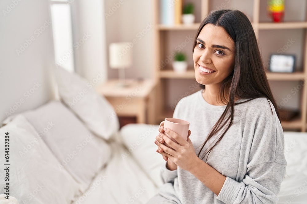 Young hispanic woman drinking cup of coffee sitting on bed at bedroom Young hispanic woman drinking cup of coffee sitting on bed at bedroom