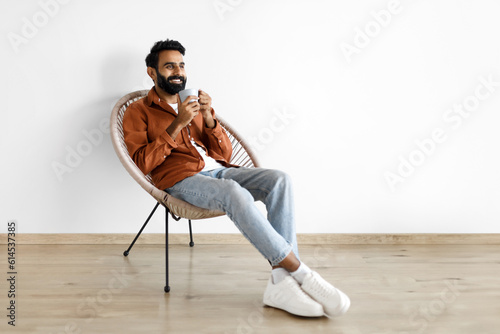 Fotografie Arabic guy with cup of coffee chilling in armchair indoors