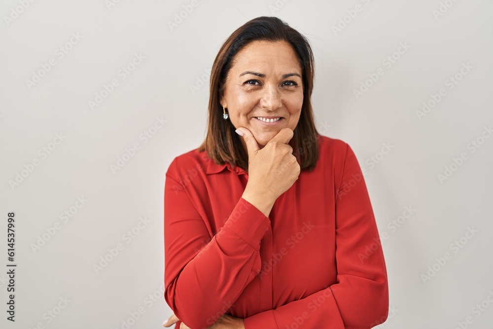 Hispanic mature woman standing over white background looking confident at the camera smiling with crossed arms and hand raised on chin. thinking positive. Hispanic mature woman standing over white background looking confident at the camera smiling with crossed arms and hand raised on chin. thinking positive.