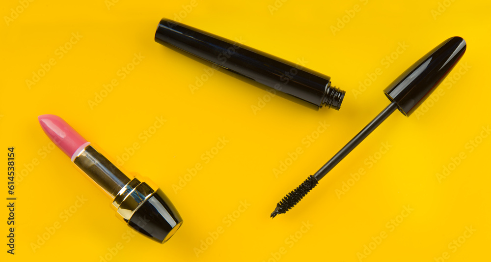 Lipstick and black mascara on a bright yellow . Wide photo.