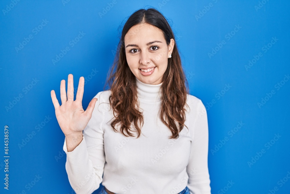 Young hispanic woman standing over blue background showing and pointing up with fingers number five while smiling confident and happy. Young hispanic woman standing over blue background showing and pointing up with fingers number five while smiling confident and happy.
