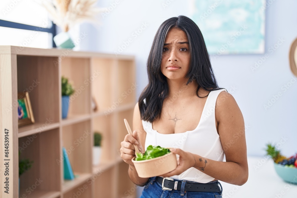 Brunette woman eating a salad at home skeptic and nervous, frowning upset because of problem. negative person. Brunette woman eating a salad at home skeptic and nervous, frowning upset because of problem. negative person.