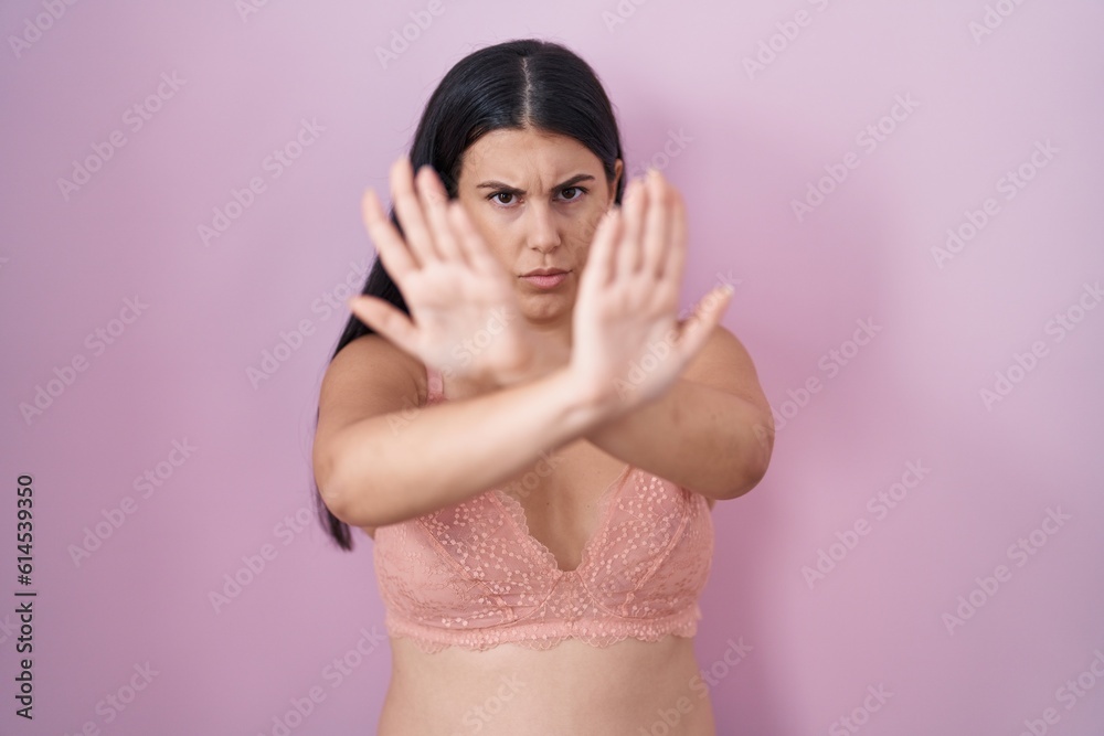 Young hispanic woman wearing pink bra rejection expression crossing arms and palms doing negative sign, angry face Young hispanic woman wearing pink bra rejection expression crossing arms and palms doing negative sign, angry face