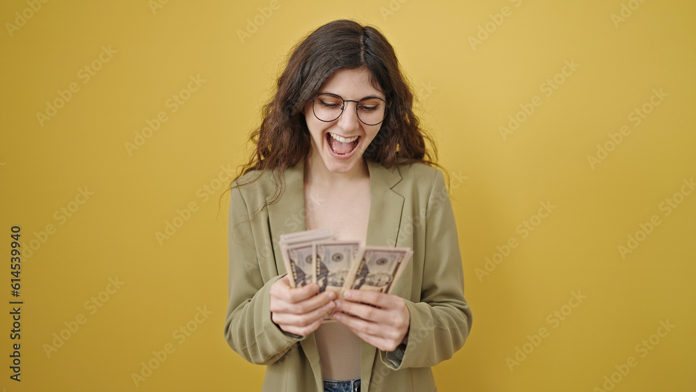 Young beautiful hispanic woman smiling confident counting dollars over isolated yellow background Young beautiful hispanic woman smiling confident counting dollars over isolated yellow background