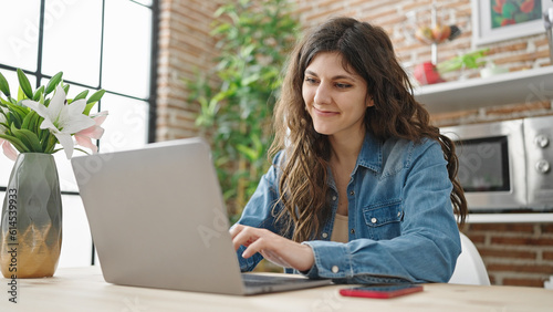 Young beautiful hispanic woman using laptop sitting on table at dinning room