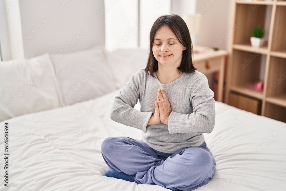 Young woman with down syndrome doing yoga exercise sitting on bed at bedroom Young woman with down syndrome doing yoga exercise sitting on bed at bedroom