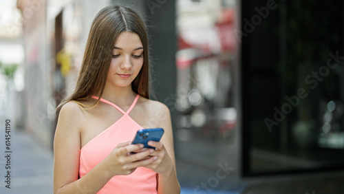 Young beautiful girl using smartphone with serious face at street