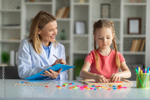 Kids Psychology. Smiling Psychotherapist Lady Taking Notes During Session With Little Girl photo