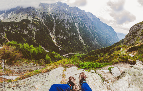 A guy sits on the top of a mountain on a rock and admires the beautiful alpine view - focus on his shoes