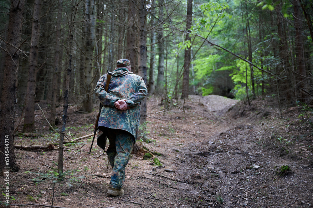 Senior hunter in a camouflage suit walking in the forest. Concept of travelling and hunting.