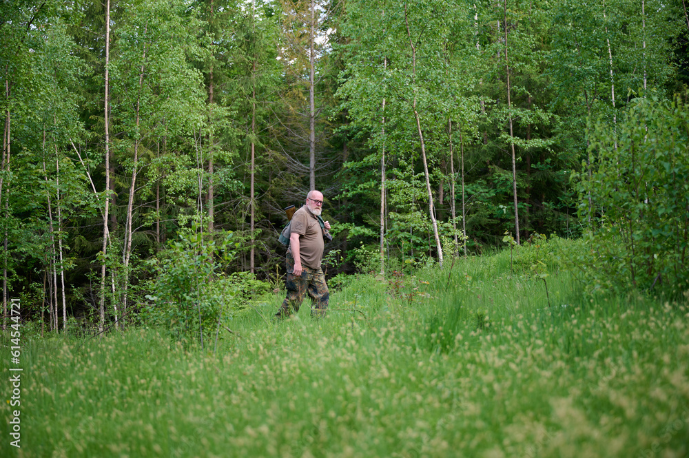 Senior hunter in a camouflage suit walking in the forest. Concept of travelling and hunting. Senior hunter in a camouflage suit walking in the forest. Concept of travelling and hunting.