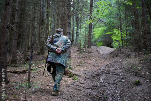 Senior hunter in a camouflage suit walking in the forest. Concept of travelling and hunting.