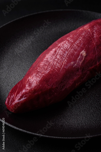 Juicy raw beef with spices, salt and herbs on a dark concrete background