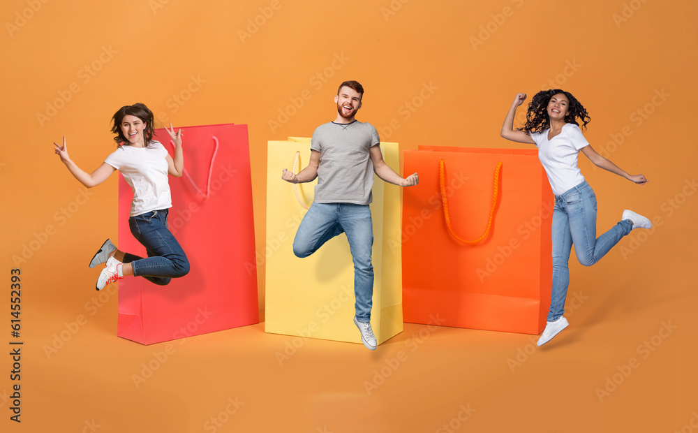 Naklejka premium Excited multiethnic millennials jumping by huge shopping bags