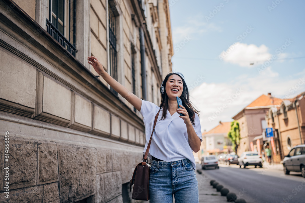 Fototapeta premium Japanese woman singing while listening music with headphones and mobile phone outside on the street