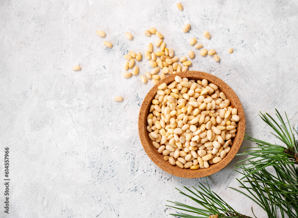Pine nuts in a wooden plate and scattered on a light texture background with branches of pine needles . The concept of a natural, organic and healthy superfood and snack. Pine nuts in a wooden plate and scattered on a light texture background with branches of pine needles . The concept of a natural, organic and healthy superfood and snack.