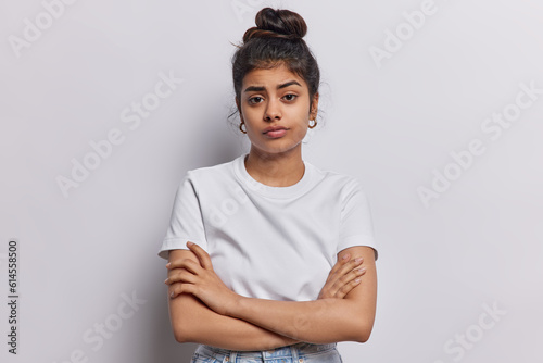 Photographie Studio shot of serious Indian woman with dark hair combed in bun keeps arms folded waits for explanations listens attentively information dressed in basic t shirt isolated over white background