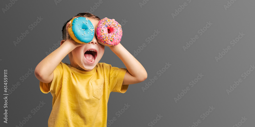 Fototapeta premium Happy cute boy is having fun played with donuts Bright photo of a child.