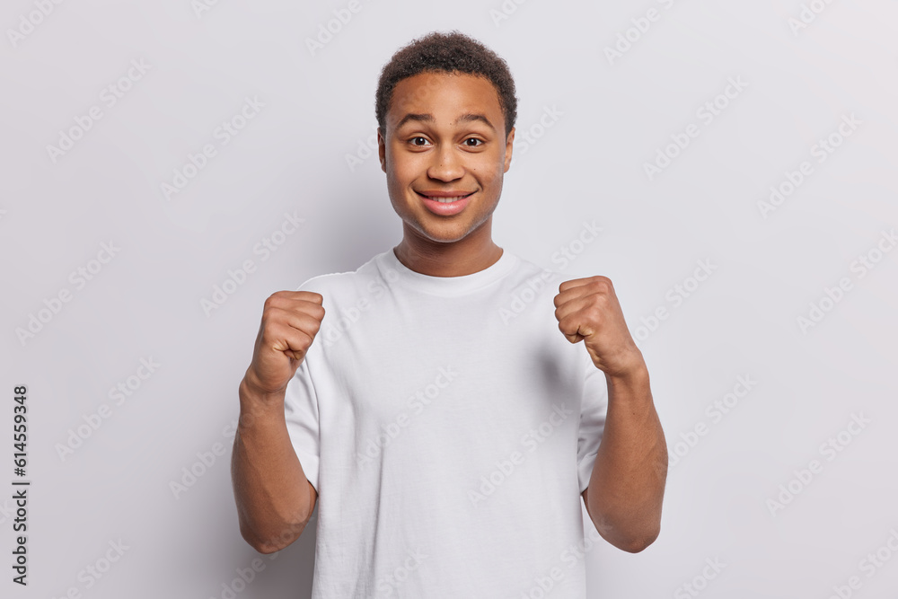 Cheerful African man in white tshirt exudes pure happiness embodying spirit of true champion who has achieved success and is ready for new triumphs clenches fists dressed casually isolated on white Cheerful African man in white tshirt exudes pure happiness embodying spirit of true champion who has achieved success and is ready for new triumphs clenches fists dressed casually isolated on white