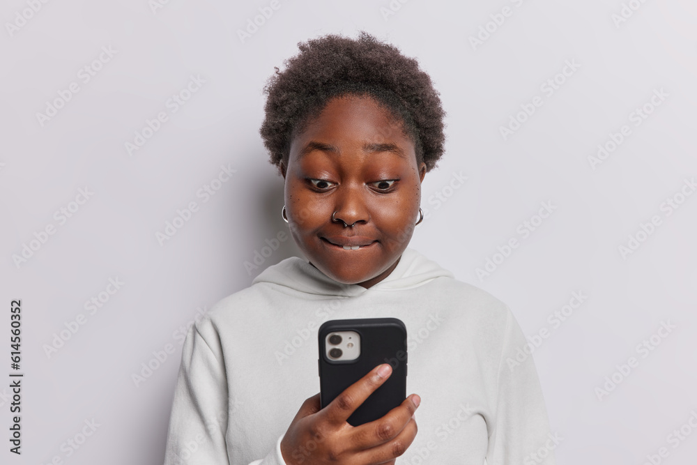 Photo of plus size dark skinned woman gazes intently at smartphone screen has eyes widen captivated by what she sees creating a moment of intrigue and curiosity wears casual hoodie isolated on white Photo of plus size dark skinned woman gazes intently at smartphone screen has eyes widen captivated by what she sees creating a moment of intrigue and curiosity wears casual hoodie isolated on white