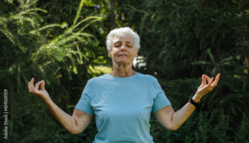 Old with short hair practicing yoga and tai chi outdoors. Elderly female meditating.