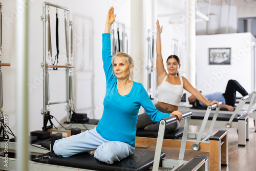 Fototapeta Naklejka Na Ścianę i Meble -  Active old woman stretching upper body practicing Pilates exercise in studio with elderly people