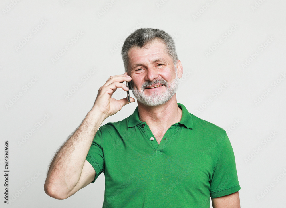 smiling senior bearded man speaking on the phone with somebody over grey background smiling senior bearded man speaking on the phone with somebody over grey background