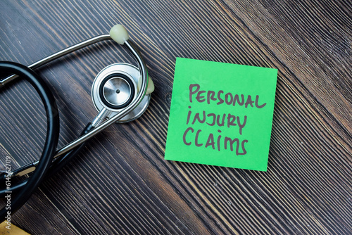 Concept of Personal Injury Claims write on sticky notes with stethoscope isolated on Wooden Table. photo