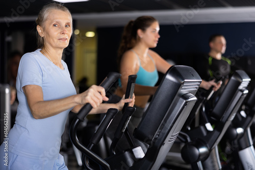 Concentrated elderly woman working out on elliptical machine in gym. Concept of healthy lifestyle of older generation
