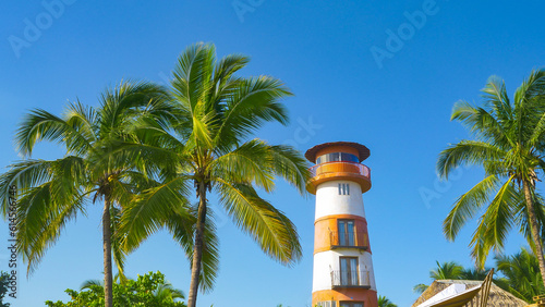 Red and white lighthouse under blue sky among coconut trees on exotic location