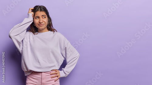 Foto Horizontal shot of confused Latin woman scratches head focused aside tries to ma
