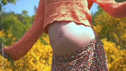 Active pregnancy.Close-up of naked belly of a pregnant woman whose happy dynamic dancing isolated on floral background at park.Cute Fun Mum Dancing.