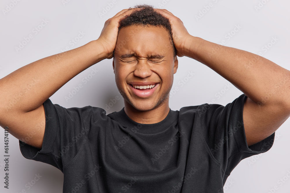 Happy African man keeps hands on head giggles positively feels overjoyed dressed in casual black t shirt cannot hide his sincere emotions isolated over white background. Happiness and joy concept Happy African man keeps hands on head giggles positively feels overjoyed dressed in casual black t shirt cannot hide his sincere emotions isolated over white background. Happiness and joy concept