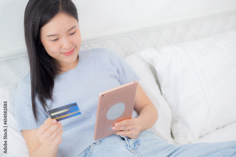Young asian woman sitting on bed using digital tablet shopping online with credit card in the bedroom at home, female paying with transaction financial, purchase and payment, business concept. Young asian woman sitting on bed using digital tablet shopping online with credit card in the bedroom at home, female paying with transaction financial, purchase and payment, business concept.