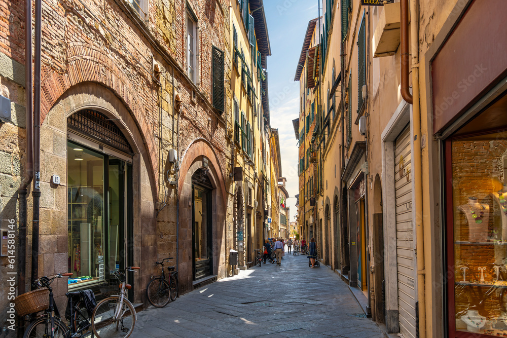 A picturesque narrow alley or street of shops, businesses and apartments in the historic center of Lucca, Italy in the Tuscany region. - obrazy, fototapety, plakaty 