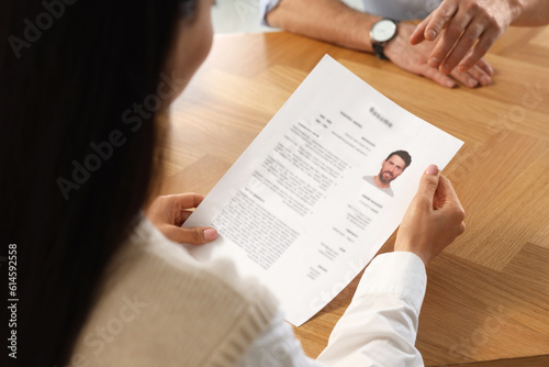 Human resources manager reading applicant's resume at wooden table, closeup