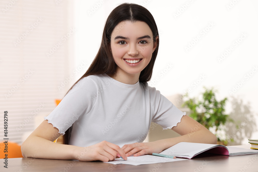 Teenage girl erasing mistake in her notebook at wooden desk indoors Teenage girl erasing mistake in her notebook at wooden desk indoors