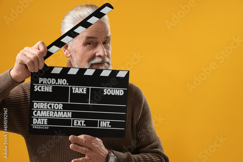 Senior actor holding clapperboard on yellow background, space for text. Film industry © New Africa