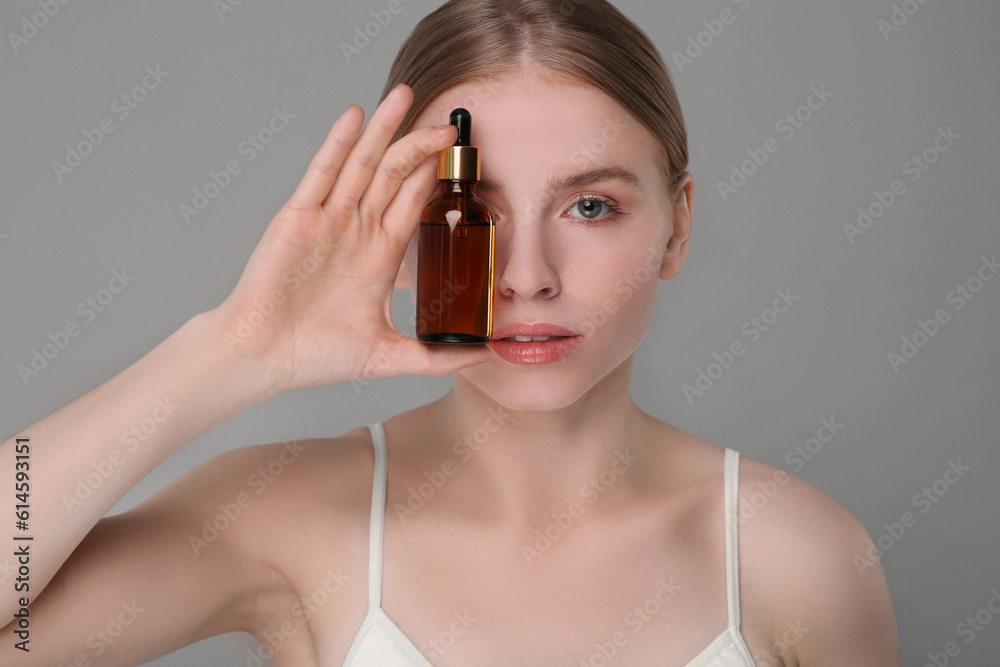 Fototapeta premium Beautiful young woman with bottle of essential oil on light grey background