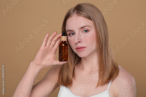 Beautiful young woman with bottle of essential oil on brown background